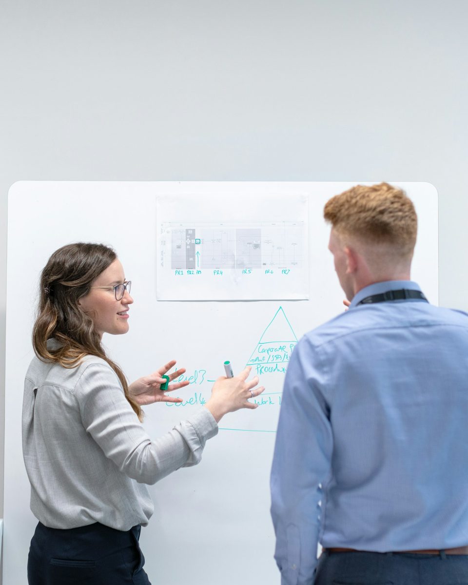 Two engineers discussing technical diagrams at a whiteboard