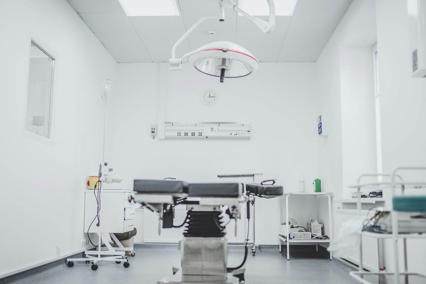 An empty operating room with a surgical lamp above the operating table and instrument trolleys